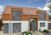 WALTHER Stylist® flad teglsten i rødbrun på et skråt tag med en attraktiv kvist på et moderne hus med træbeklædning