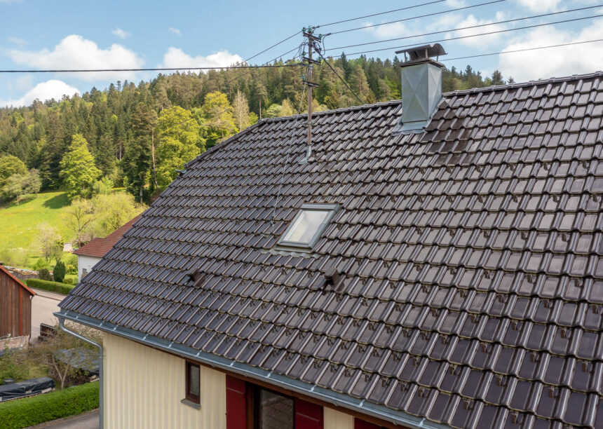 Krüppelwalmdach mit J11v in edelbraun auf saniertem Wohnhaus mit Sanilüfter und First F6v im Fokus.